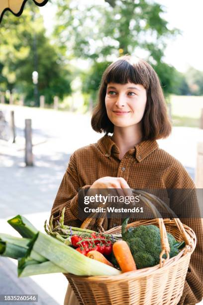happy woman wearing brown shirt holding basket of vegetables at farmer's market - leek stock pictures, royalty-free photos & images