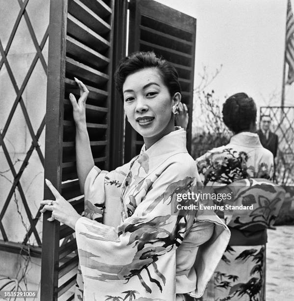 American actress Miko Taka wearing a traditional Japanese costume while holding a shutter in front of an outdoor mirror, February 4th 1958.