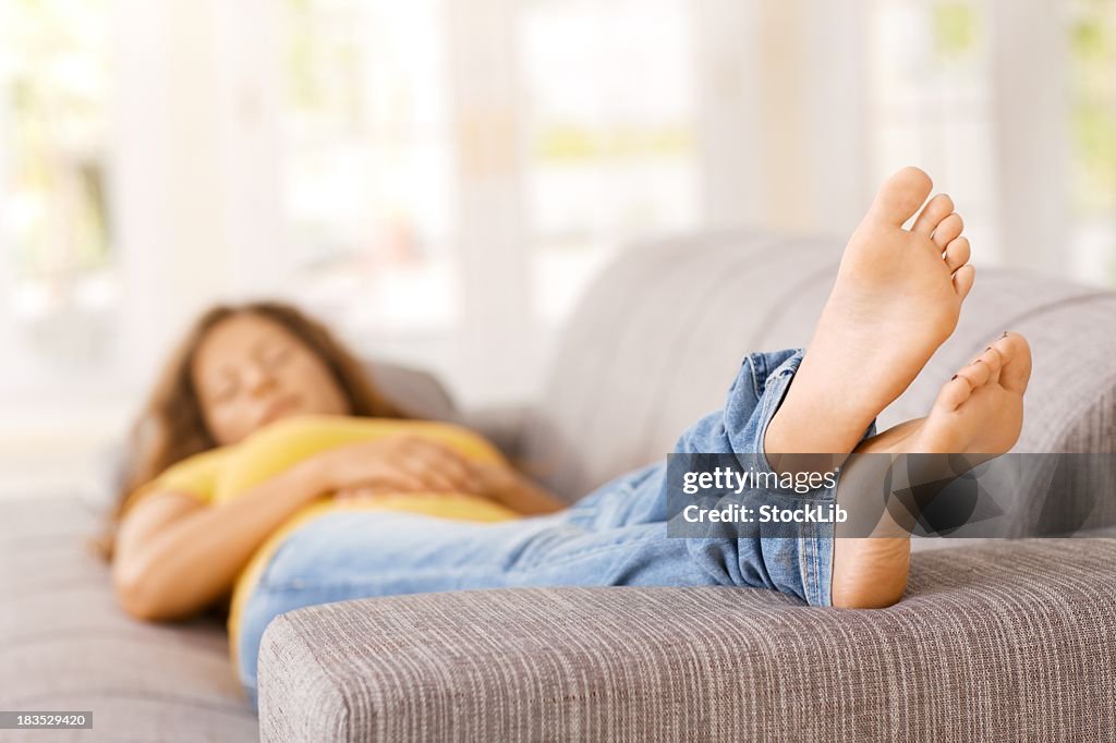 Young woman lying on sofa in living room, sleeping