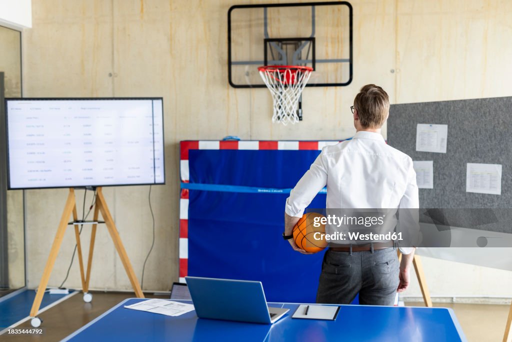 Businessman standing with basketball in front of hoop and device screen