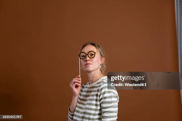 confident woman holding eyeglasses prop over brown background - arrogance stock pictures, royalty-free photos & images