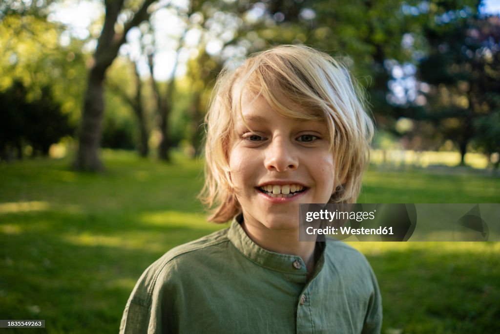Smiling blond boy in front of trees at park