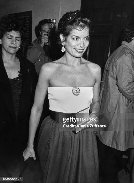 Nicaraguan actress Bianca Jagger wearing a white tube top, featuring a circular brooch mounted centrally on her chest, attends an event, United...