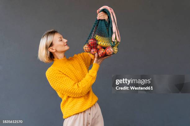 smiling woman looking at mesh bags with fruits against black background - reusable bag isolated stock pictures, royalty-free photos & images