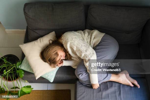 woman with stomachache sleeping on sofa at home - curled up on sofa stock pictures, royalty-free photos & images