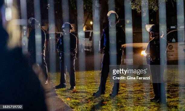 Los Angeles police officers in tactical gear maintain a line on the other side of a perimeter fence to keep members of the Palestinian Youth Movement...