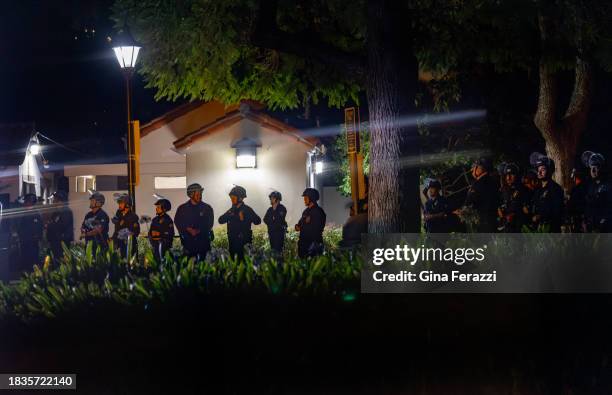 Los Angeles police officers in tactical gear maintain a line on the other side of a perimeter fence to keep members of the Palestinian Youth Movement...