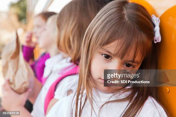 depressed little girl leaning on school bus with other students - no confidence stock pictures, royalty-free photos & images
