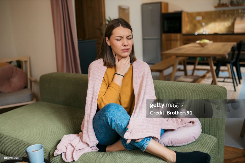 Caucasian woman suffering from sore throat sitting on sofa