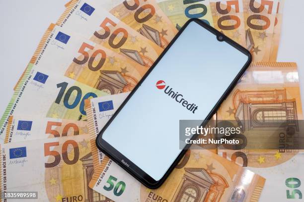 The UniCredit logo is being displayed on a smartphone screen with 50 and 100 Euro bills in Athens, Greece, on December 9, 2023.