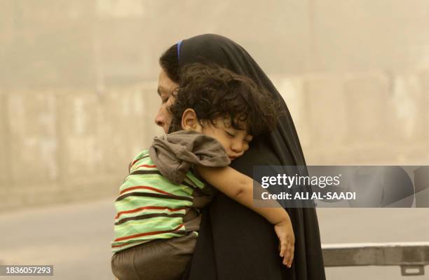 An Iraqi woman carries her sleeping son while walking in the soaring heat as Baghdad witnesses a severe heat wave and sand storms on July 21, 2010....