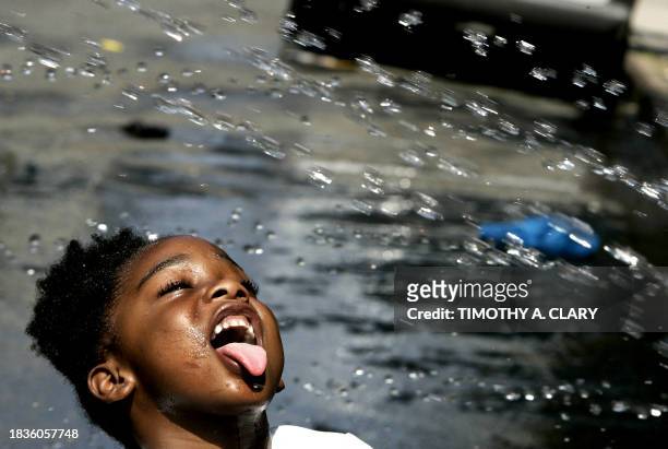 Young girl sticks her tongue out to get a drink as kids play in a open hydrant in Harlem to beat the heat 01 August 2006 in New York. New York,...