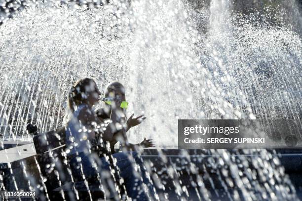 Girl drinks lemonade with her girlfriend as they refresh themselves by fountains in Kiev 04 August 2003.