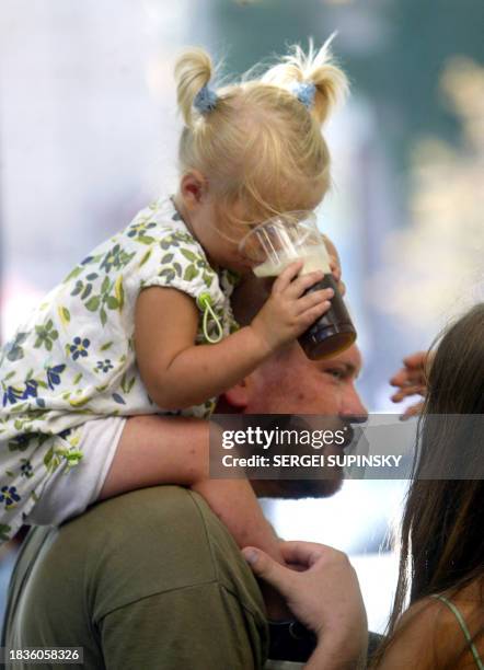 Girl drinks lemonade as she sits on her father's shoulders during hot day in Kiev 01 August, 2005. The over 37 C, hottest weather for the last 30...