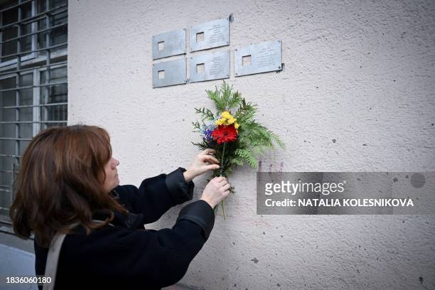 This photograph taken on November 9, 2023 shows Oksana Motievskaya, coordinator of the "Last Address" Foundation, leaving flowers under metal...