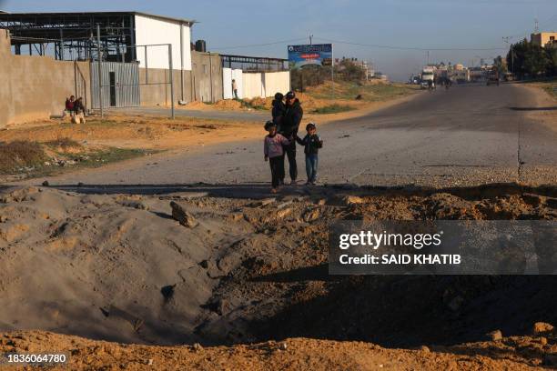 Palestinians fleeing Khan Yunis in southern Gaza Strip further south toward Rafah, stare at a crater caused by Israeli bombing on the Salah Al-Din...