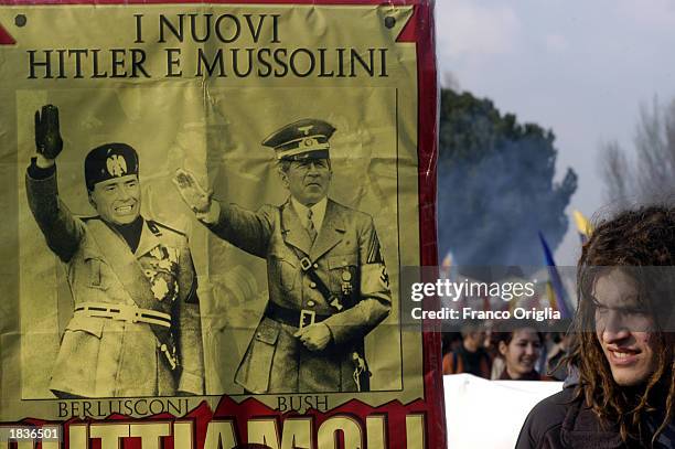 An antiwar activist stands near a sign which compares U.S. President George W. Bush and Italian Prime Minister Silvio Berlusconi to Hitler and...