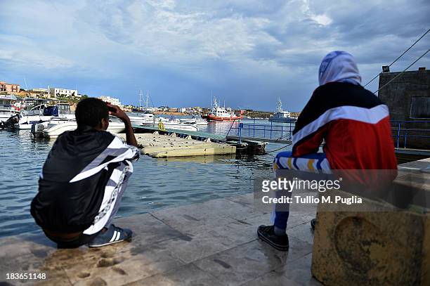 Survivors of the shipwreck of immigrants off the Italian coast sit near the water of Lampedusa on October 8, 2013 in Lampedusa, Italy. The search for...