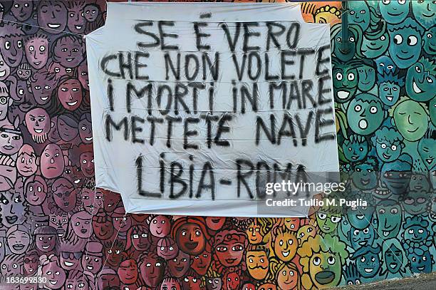 Banner which translates as 'If it is true that you do not want the dead in the sea, create a ship line from Libya to Rome' is displayed at Lampedusa...