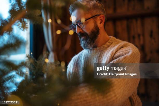 handsome mature man getting ready for christmas, new year's eve celebrations in cabin in mountains. untangling christmas lights, decorating christmas tree. concept of hygge winter, peaceful, cozy moments for yourself. - endast en man bildbanksfoton och bilder