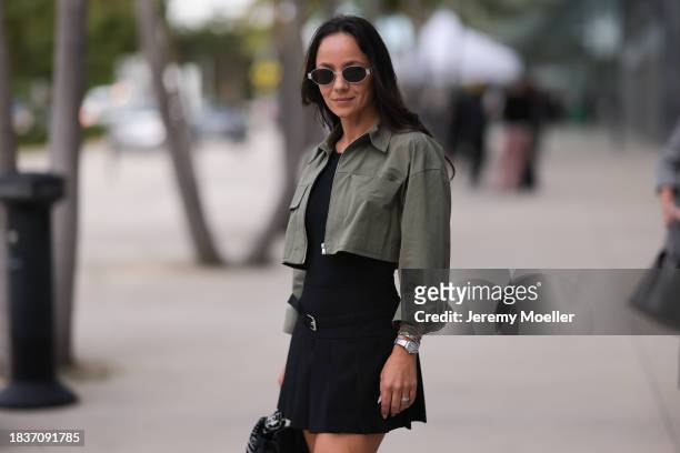 Eden Lotenberg seen wearing Celine Triomphe silver sunglasses, black cotton top, matching black pleated short skirt with a belt detail, khaki green...