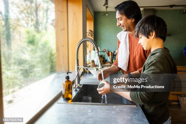 father and teenage son washing dishes in kitchen - poetshulp stockfoto's en -beelden
