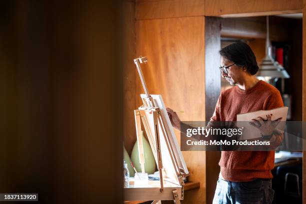 middle age man painting on easel at home - canvas stand stock pictures, royalty-free photos & images
