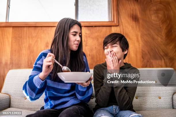 teenage siblings eating breakfast cereal on sofa at home - syskon tonåring bildbanksfoton och bilder