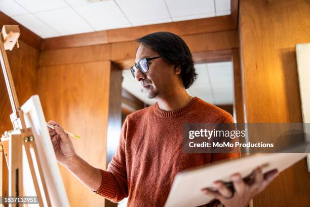 middle age man painting on easel at home - canvas stand stock pictures, royalty-free photos & images