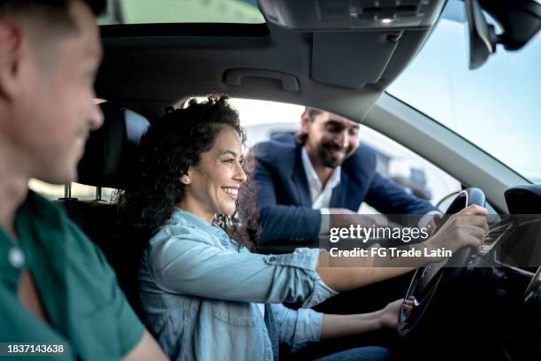 car salesman showing a car to customer couple at dealership - car buying stock pictures, royalty-free photos & images