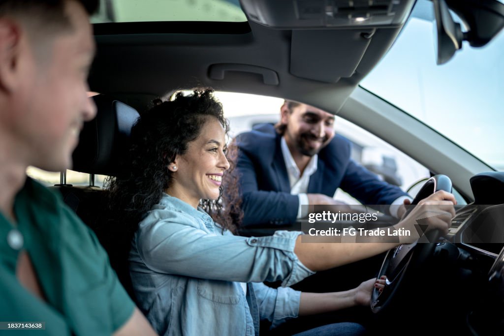 Car salesman showing a car to customer couple at dealership