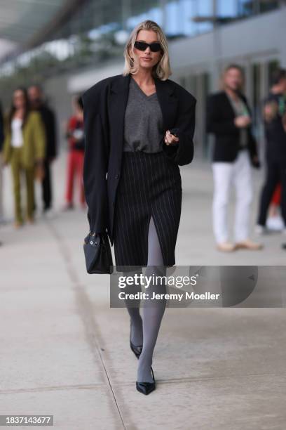 Elsa Hosk seen wearing Balenciaga black sunglasses, gold statement earrings, grey v-neck wool knit jumper, black pinstriped slit midi skirt, black...