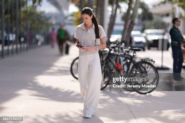 Yana Kotina seen wearing Cartier Love yellow gold chain / necklace, beige cotton polo shirt, white wide leg pants, YSL cream white / beige leather...