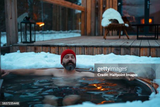 man bathing in wood-burning hot tub, enjoying hot water during cold, snowy winter evening. unique bathing experience during relaxing winter weekend in cabin in mountains. concept of hygge winter, peaceful, cozy moments for yourself. - fireplace forest stock pictures, royalty-free photos & images