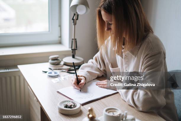 young woman jewelry designer artist drawing sketch on paper working at desk in the studio - scissors paper stone stock pictures, royalty-free photos & images