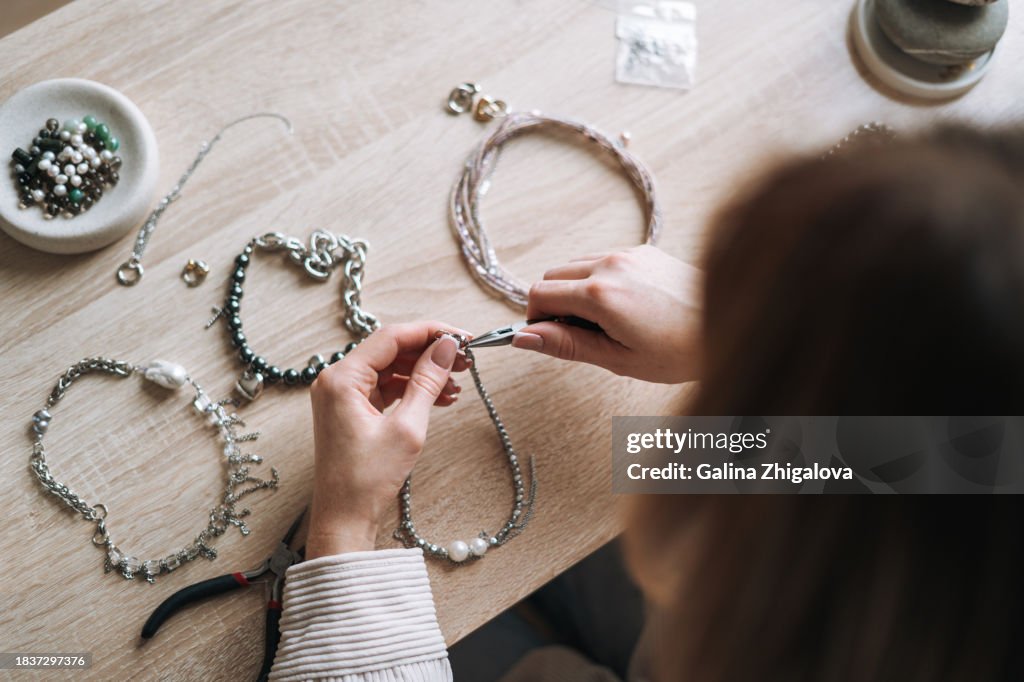Young woman jewelry designer creating necklace and working at table in the studio