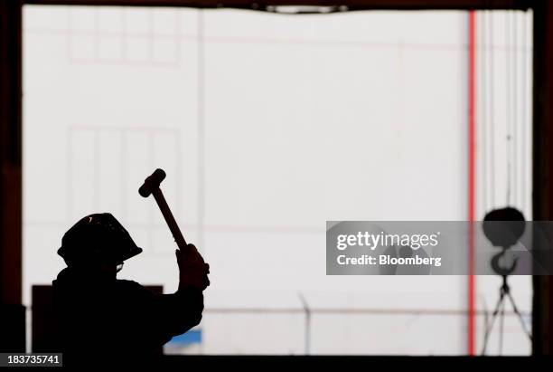 The silhouette of a worker is seen using a mallet while welding a portion of a barge under construction at the Seaspan Vancouver Shipyard in North...