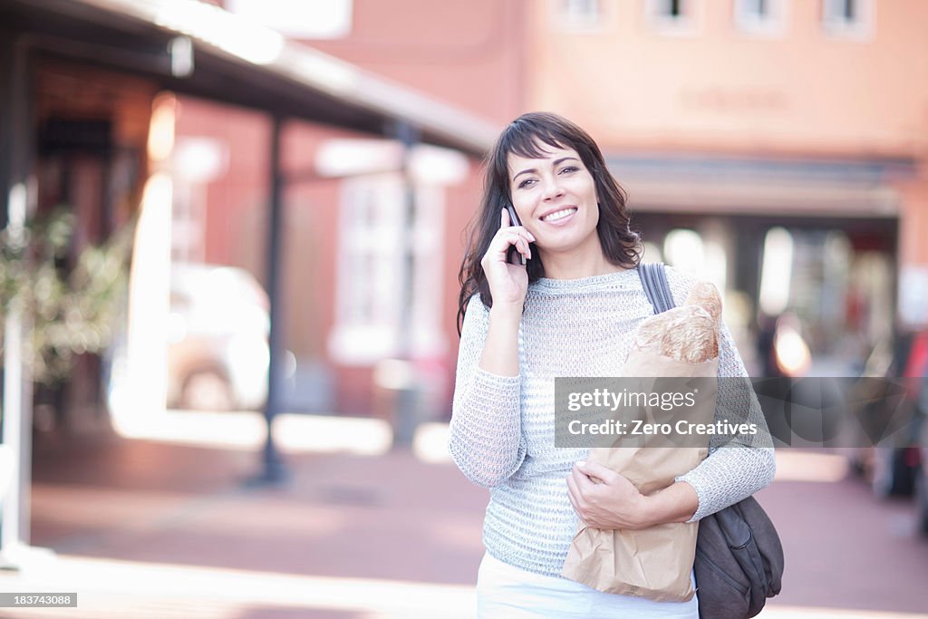 Mid adult woman on cell phone with bread