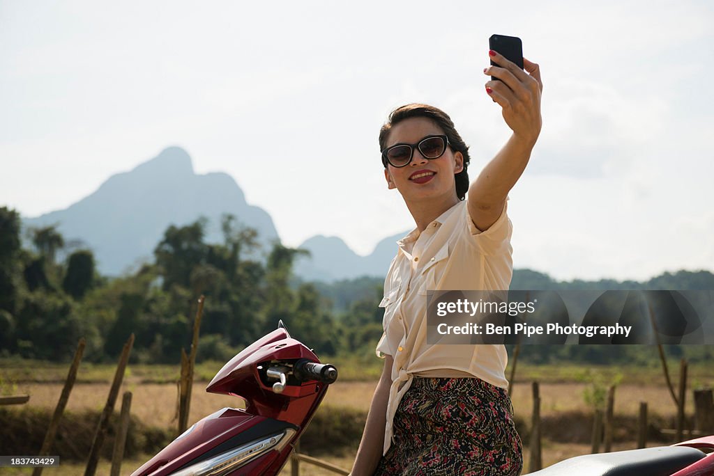 Woman photographing self on moped, Vang Vieng, Laos