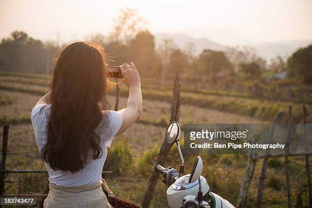 woman on moped taking photograph in rural scene - alleen mid volwassen vrouwen stockfoto's en -beelden