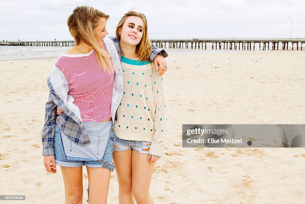 Girlfriends standing on beach with arm around