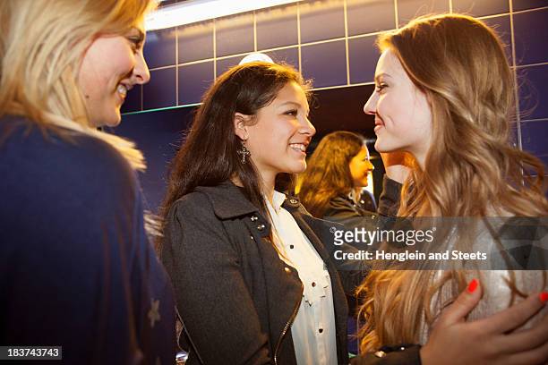 three teenage girls chatting and smiling in toilets - nightclub bathroom stockfoto's en -beelden