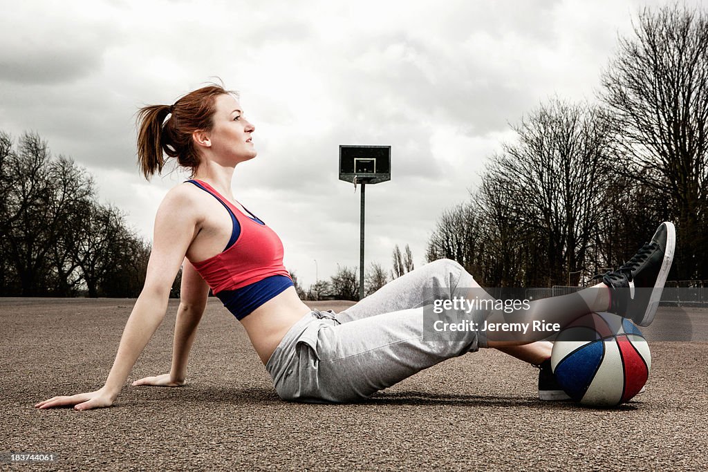 Woman with ball under one leg sitting on court