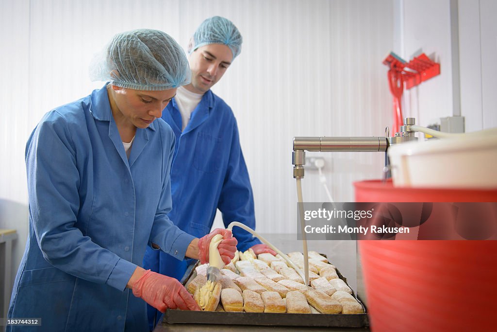 Baker guiding trainee in adding cream to freshly baked cakes