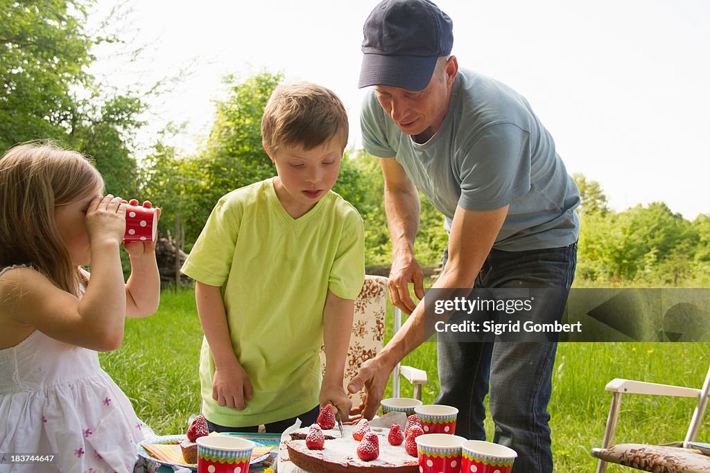 Father with two children cutting birthday cake outdoors