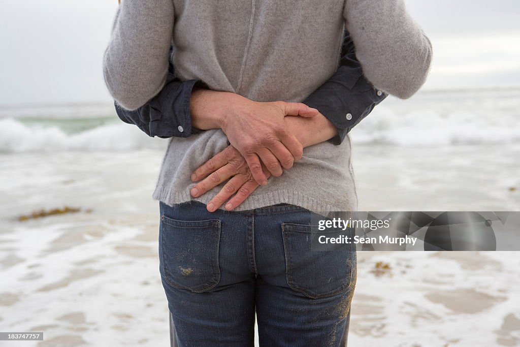 Mature couple embracing on beach, mid section