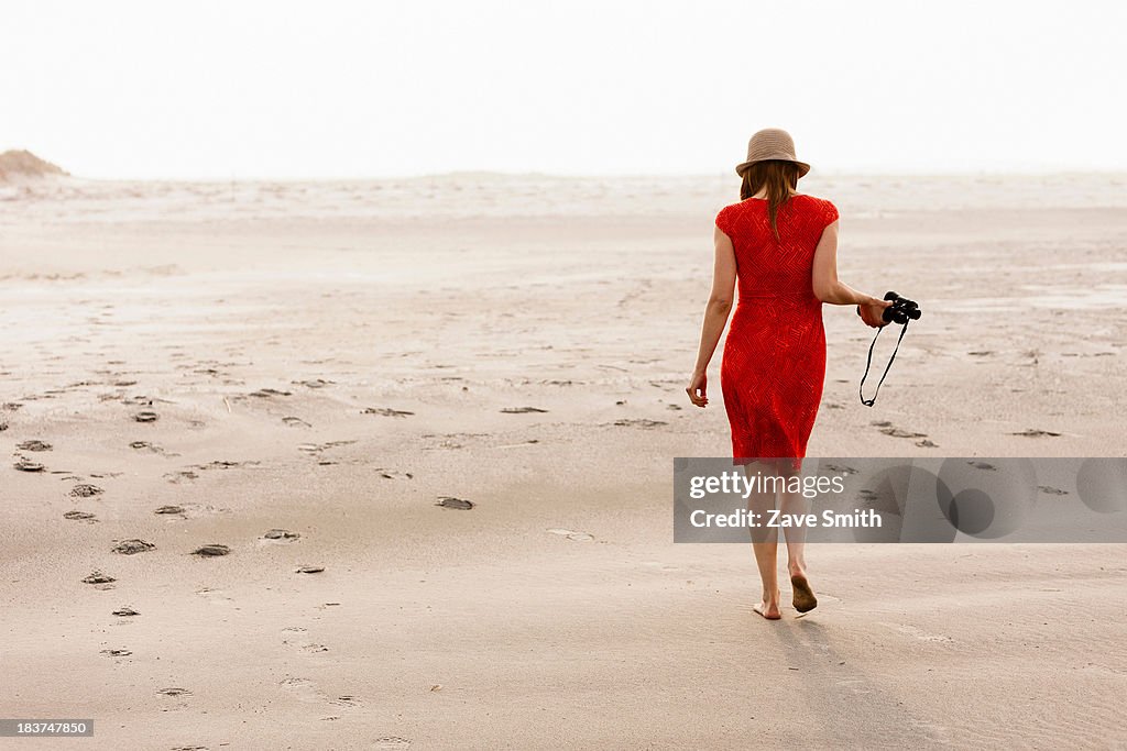 Mature woman wearing red dress walking on beach