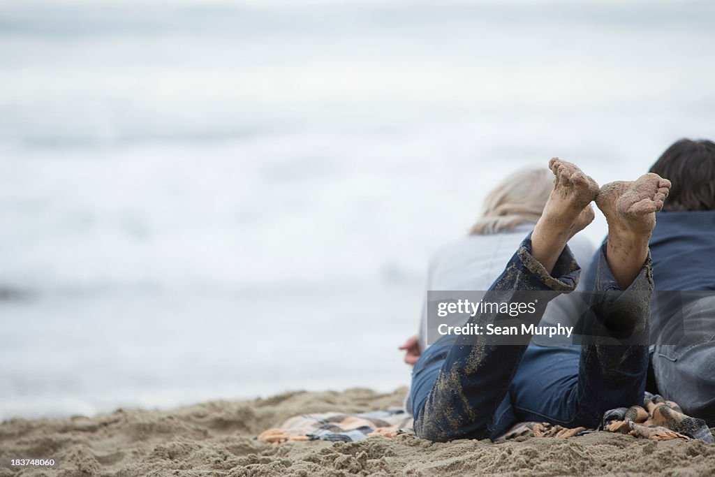 Mature couple lying on beach looking at sea