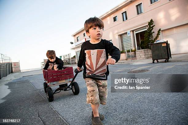 boy pulling brother along in cart - child-pulling-wagon stock pictures, royalty-free photos & images