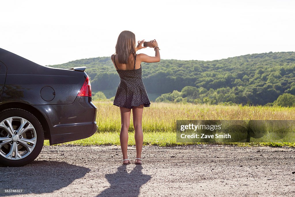 Young woman photographing rural scene with camera phone